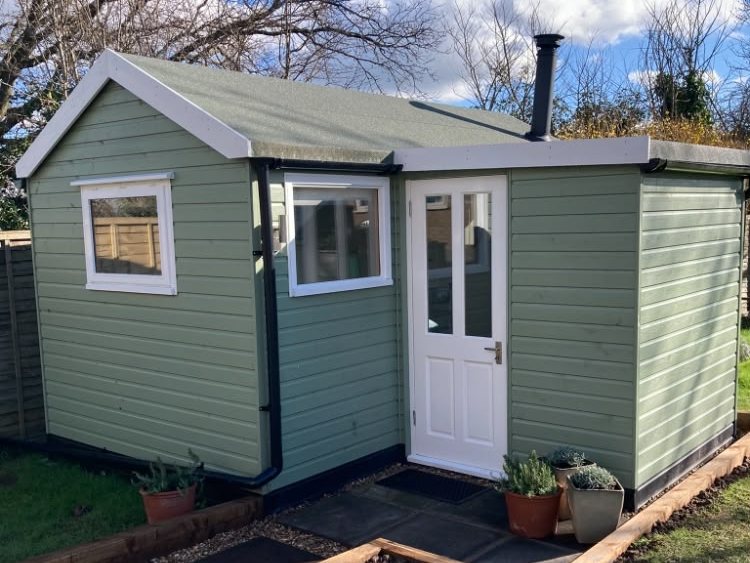 The Beauty Culture cabin — sage green with a white front door and potted plants beside the step